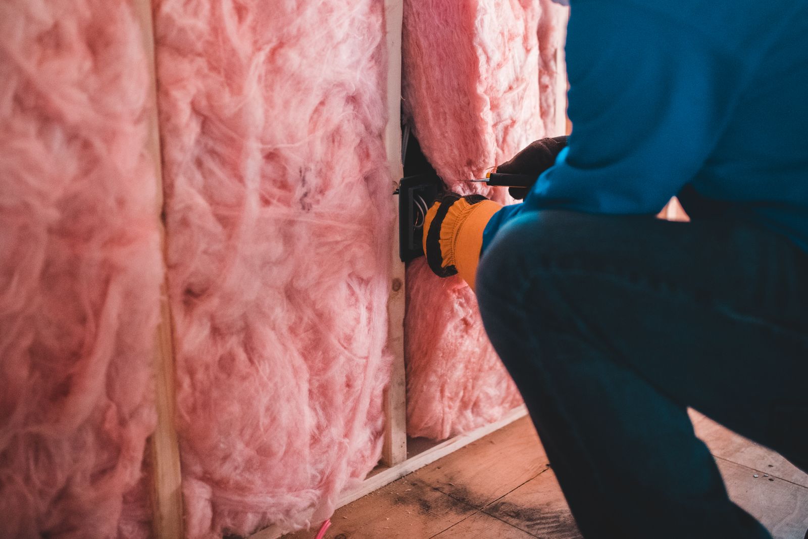 An installer fitting mineral wool insulation between wall studs